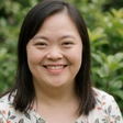 A woman with Down syndrome smiling warmly in a garden, a member of the OpenHeartMatch community